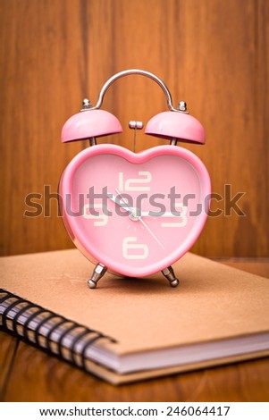 Pink heart shape alarm clock on notebook