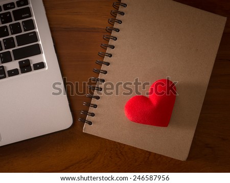 Concept laptop PC with book and red heart on office wood table.