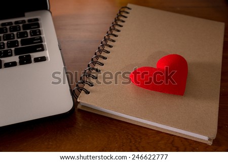 Concept laptop PC with book and red heart on office wood table.