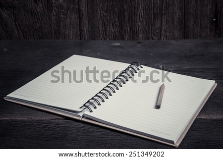Notebook and pencil on wood table. Black and white image.