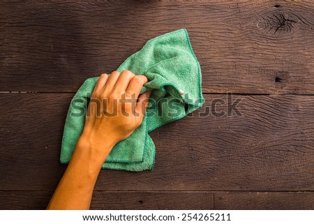 Hand with old green cleaning rag on wood background.