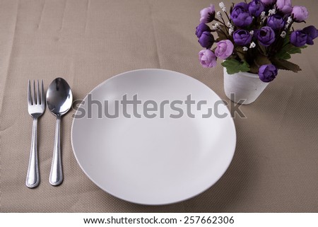 Empty dish and violet flower on dinner table.