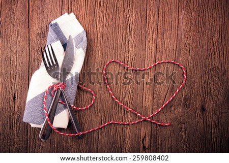 Silverware on wood table with heart shape red rope. Concept valentine day background.