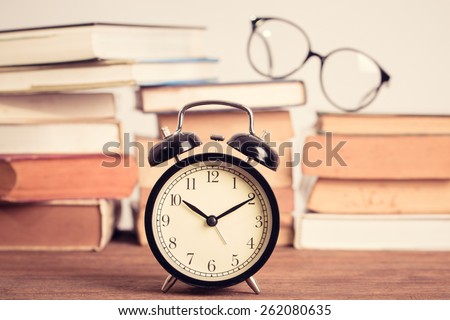 Education concept. Eyeglasses with Alarm clock with old books on table . Vintage filter