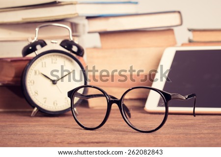 Education concept. eyeglasses with Alarm clock with old books on table with Tablet PC . Vintage filter