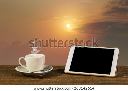 Hot coffee with tablet PC on table. With beautiful sunrise background.
