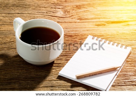 Fresh morning with black coffee with note paper and pencil on wood table. Vintage light filter.