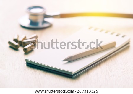 Medical concept. Notebook with pencil on table with herb capsule and stethoscope background. Vintage filter.