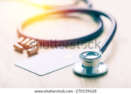 Medical concept. Credit card on table with herb capsule and stethoscope background. Vintage filter.