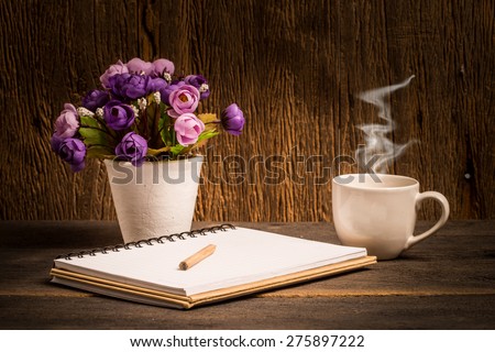 Hot coffee with open book and flower in vase decor on table.