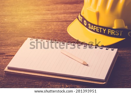 Yellow Safety Helmet Hat with SAFETY FIRST word tag and notebook on Wood background. Vintage filter