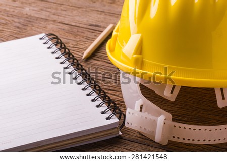 Yellow Safety Helmet Hat with SAFETY FIRST word tag and notebook on Wood background.