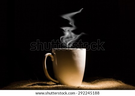 White mug of hot coffee or hot drink in dark.