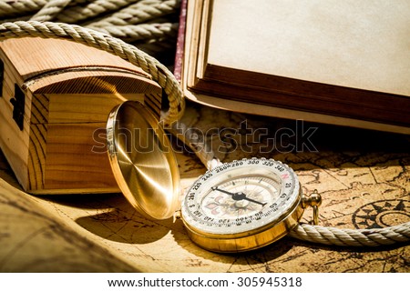 Vintage compass on map with blank old book and rope and treasure chase.