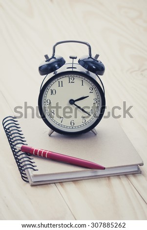 alarm clock on book and pen on office table. Retro filter