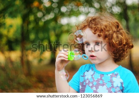 Portrait of happy curly little girl blowing soap bubbles