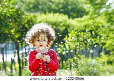 Beautiful little curly girl blowing dandelion