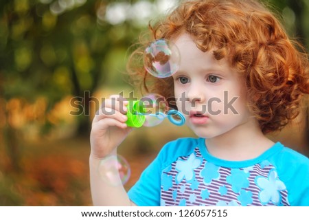 A  little girl blowing soap bubbles, closeup portrait beautiful curly baby.