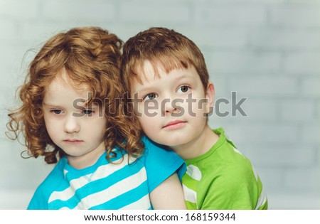 Little brother hugging sister, close-up portrait on a light background.