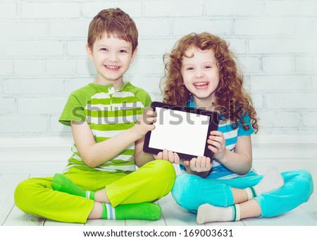 Twins boy and girls with the tablet PC on a light background. Holding thumbs up.