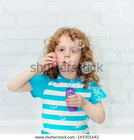Curly girl blowing soap bubbles, on a light background in the studio.