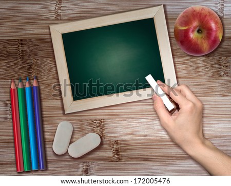 Hand with chalk  lie on a wooden table with pencils, erasers and a red apple.  Education concept.