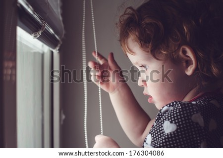 Little kid on the window blinds open.