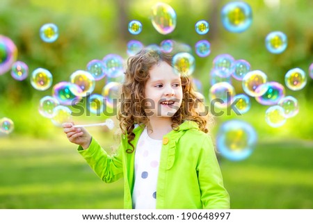 A little girl blowing soap bubbles, spring portrait beautiful curly hair.