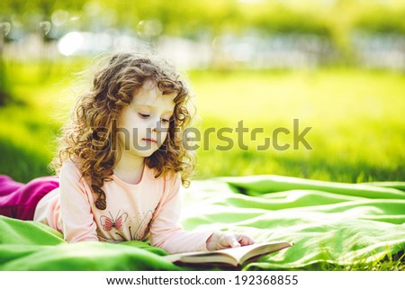 Little girl reading a book in the spring park, toning photo.