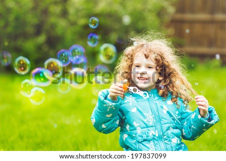A little girl blowing soap bubbles, closeup portrait beautiful curly baby.