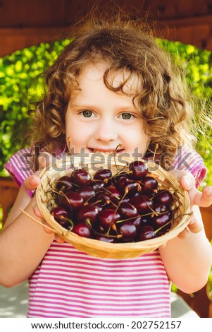 Beautiful little girl holding a basket of sweet cherries.