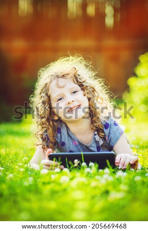 Little girl lying on the grass and holds in hands tablet pc. Toning photo.