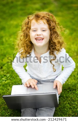 Happy surprised child with laptop sitting on the grass.