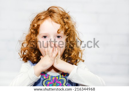 Little girl covering her mouth with her hands. Surprised or scared. On the light background indoors.