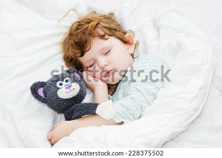 Sweet child is sleeping with a toy in bed.
