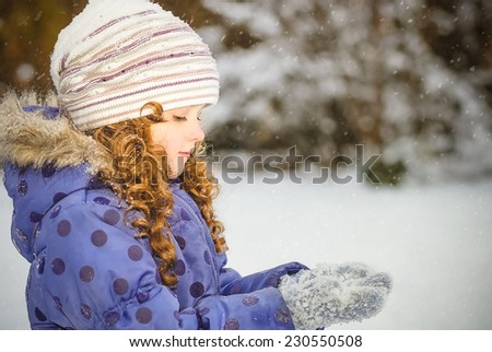 Little girl stretches her hand to catch falling snowflakes. Winter portrait.
