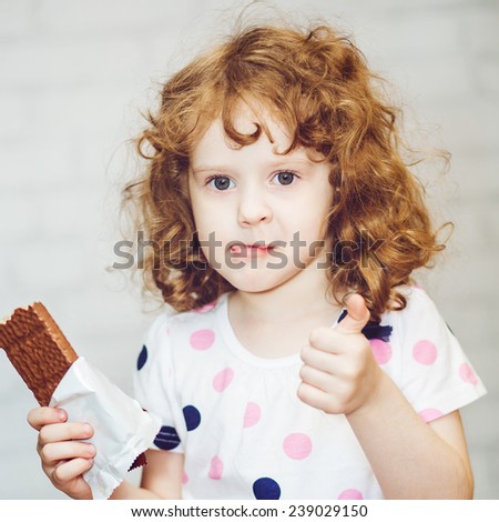 Little girl greedily holding chocolate and licks his lips.