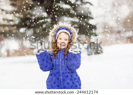 Surprised funny girl raised her hands in the air, catching snowflakes in winter park.