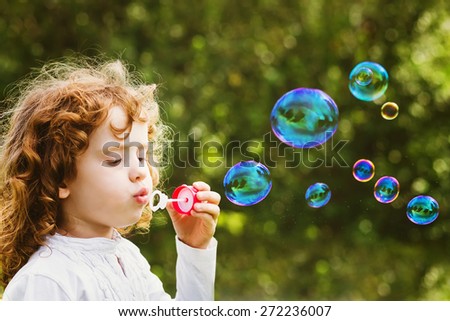 A little girl blowing soap bubbles, closeup portrait beautiful curly baby