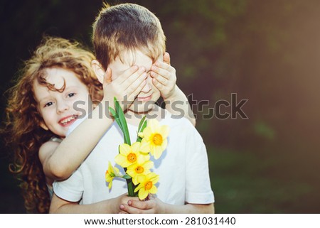 Beautiful girl covering her boyfriend\'s eyes and boy with bouquet flowers in his hand. Toned for instagram filter. Focus for boy.
