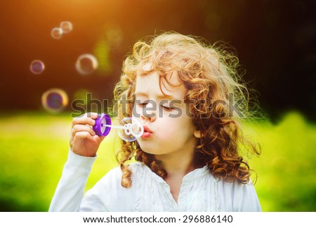 A little girl blowing soap bubbles in summer park. Background toninf for instagram filter.