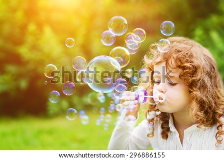 A little girl blowing soap bubbles in summer park. Background toninf for instagram filter.
