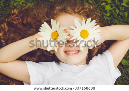 Child with daisy eyes, on green grass in a summer park.