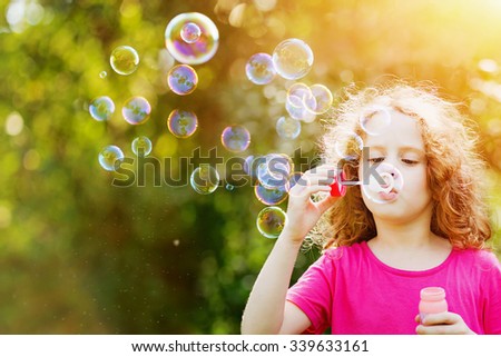 Curly girl blowing soap bubbles in summer park.