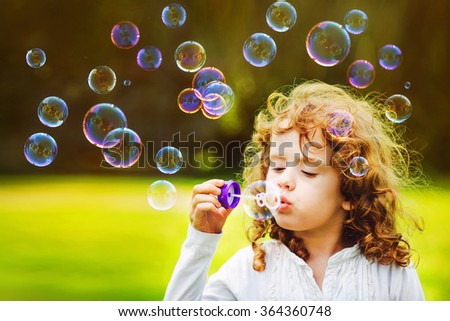 little girl blowing soap bubbles in summer park. Background toning for instagram filter.