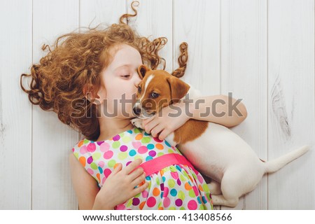 Little girl and her puppy whispers on wood background.