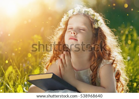 Little girl folded her hand and close your eyes in praying, dreaming in park outdoors.