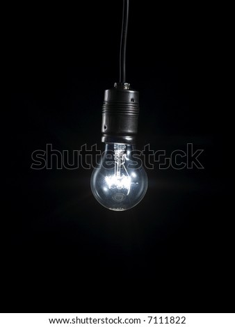 A glowing light bulb in the darkness hanging on a cable.