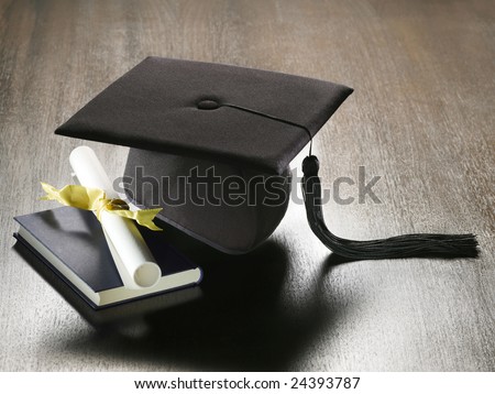A view of several items related to education and graduation including a graduation cap with tassel, a book and a rolled up diploma