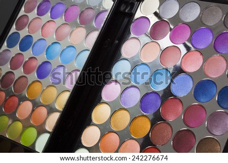 Colorful display of eye makeup in an open portable compact with eye shadow in all the colors of the spectrum, also reflected back in the mirror in the lid